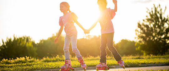 Two girls hold hands as they skate on summer day