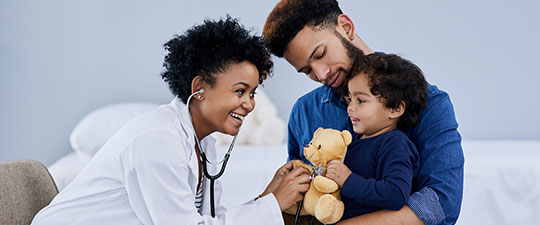 Female doctor smiling as she checks child's stuffed animal and father looks on