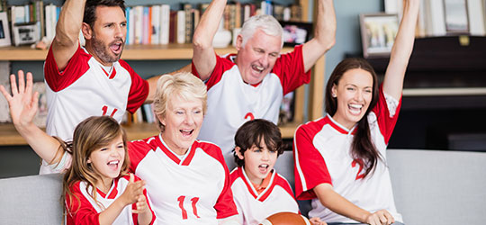 Multi-generational family wearing red and white football jerseys cheer on their team together. 
