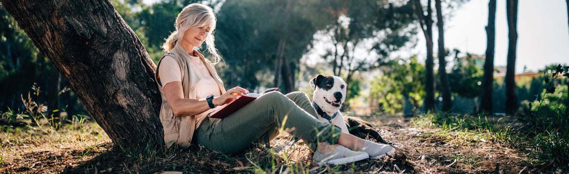 senior woman reading a book outside with her dog