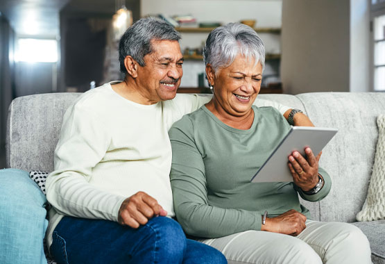senior couple sitting on couch while viewing tablet together