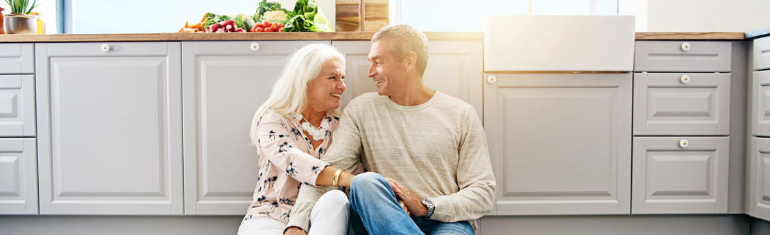 senior couple smiling while sitting on kitchen floor