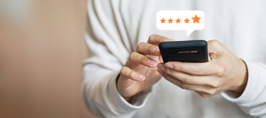 Unidentifiable person using their phone to rate a business. Five orange stars appear above the phone