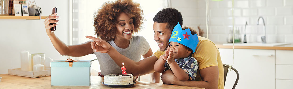 Young family takes a selfie at the kitchen table while celebrating son's second birthday.